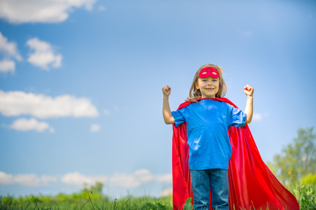 Funny little girl playing power super hero over blue sky background. Superhero concept.の写真素材