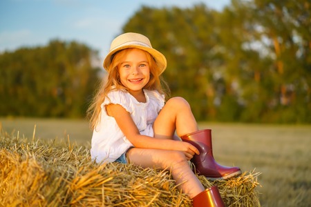 Little girl in a field with hay rolls at sunsetの写真素材