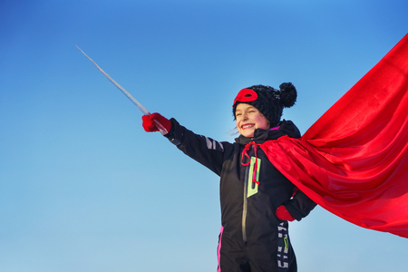 Funny little girl playing power super hero over blue sky background. Superhero concept.の写真素材