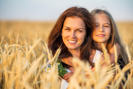 Young mother and her daughter on golden wheat field at summer evening.の写真素材