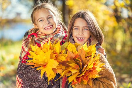 Two cute smiling 8 years old girls posing together in a park on a sunny autumn day. Friendship concept.の写真素材