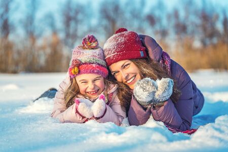 Little girl and her mother playing outdoors at sunny winter day. Active winter holydays concept.の写真素材