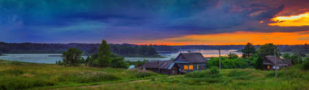 Panoramic view on dramatic sunset over lake and old village in countryside