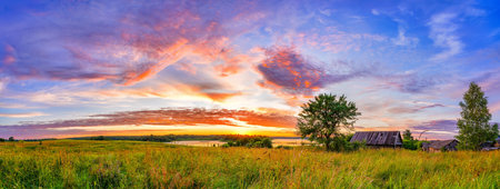 Panoramic view on sunset over old wooden hut and lonely tree in countrysideの写真素材