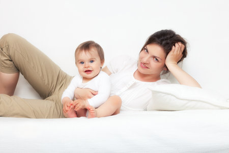 Happy mother playing with baby on white sofaの写真素材