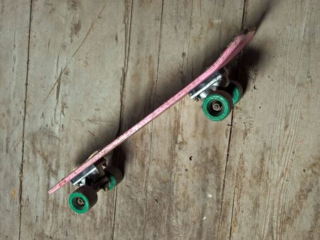 Old battered skateboard on a wooden background.