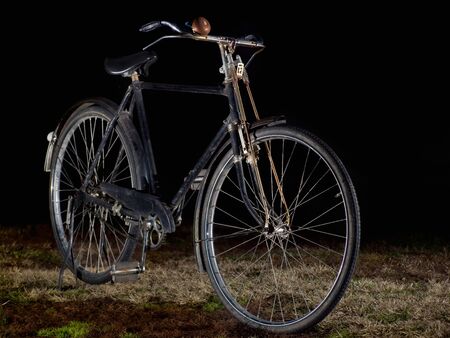 Old-fashioned black bicycle on a dark background.