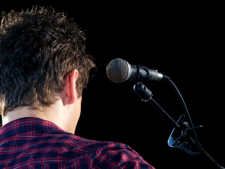 Young musician with his microphone on a dark background.の写真素材