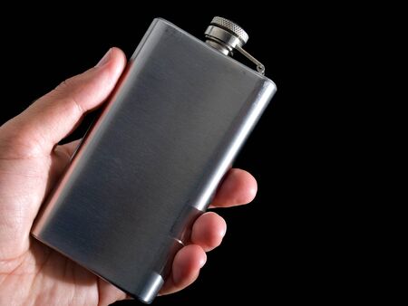 Man is holding hip flask in his hand on a black background.の写真素材