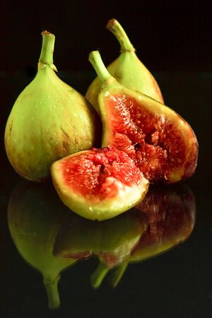 Green figs on a black background with a reflection at the bottomの写真素材