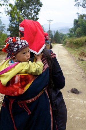 SAPA, VIETNAM - NOV 22: Unidentified young girl from the Red Dao Ethnic Minority People carries a baby on November 22, 2010 in Sapa, Vietnam. Red Dao are the 9th largest ethnic group in Vietnam のeditorial素材