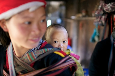 SAPA, VIETNAM - NOV 22: Unidentified young girl from the Red Dao Ethnic Minority People carrying baby on November 22, 2010 in Sapa, Vietnam. Red Dao are the 9th largest ethnic group in Vietnamのeditorial素材
