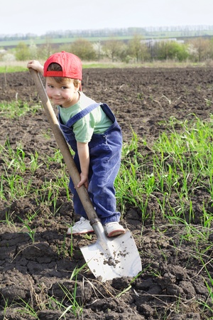 Little boy on field with big shovel, looking to cameraの写真素材
