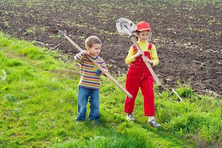 Two little children walking on field with garden toolsの写真素材