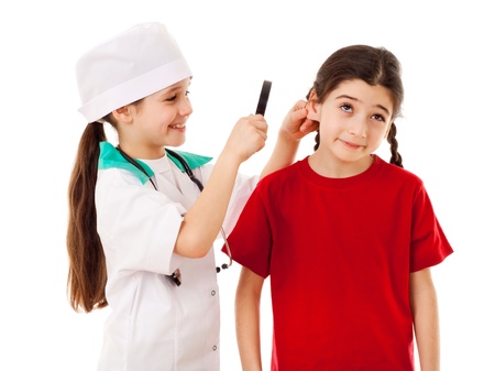 Little girl in doctor costume are inspecting the another girl s ears with magnifier, isolated on whiteの写真素材