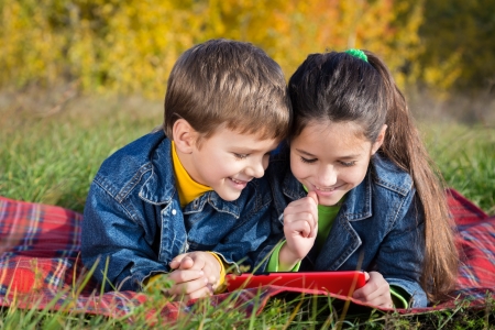 Two smiling kids with tablet pc on the autumn landscape, outdoorsの写真素材