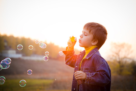 Smiling boy blowing the soap bubbles on the autumn landscape against sunsetの写真素材