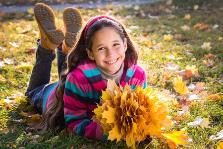 Smiling girl lying on grass with autumn leavesの写真素材