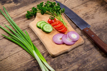 cutting board on table with greens and vegetablesの写真素材