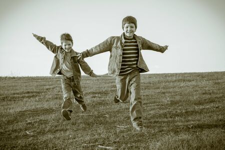 Two happy boys running together on hill, sepia toned