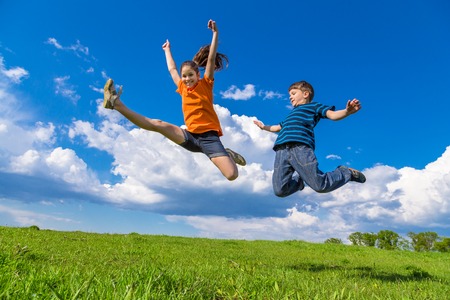 Two happy kids jumping on green hills against blue skyの写真素材