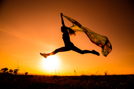 silhouette of  jumping girl on hill against sunsetの写真素材