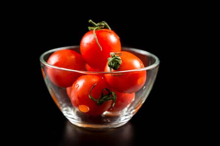 Wet cherry tomatoes in glass bowl on black backgroundの写真素材