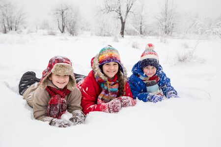 Three kids lying down together on white snowの写真素材