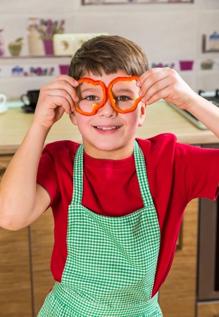Funny adorable boy with sliced paprika on eyesの写真素材