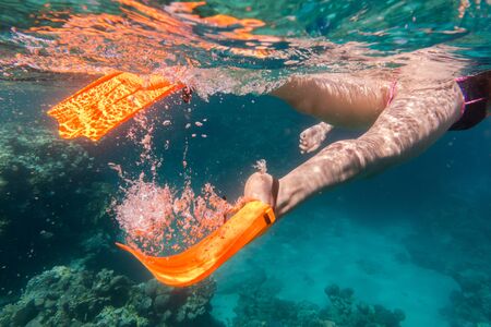 Girls legs in orange flippers underwater in sea near coral reefの写真素材