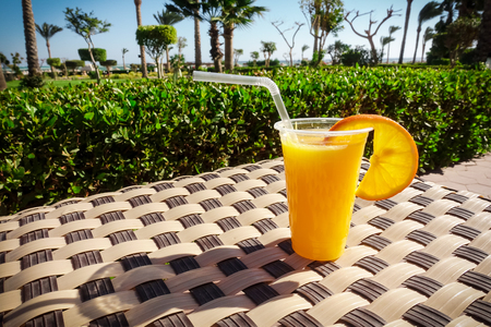 Fresh orange juice in plastic glass on table with view to gardenの写真素材