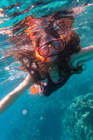Girl in swimming mask diving in sea near coral reefの写真素材