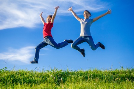 Two kids jumping on green hills against blue skyの写真素材