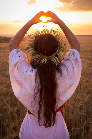 young girl on wheat field making heart symbolの写真素材