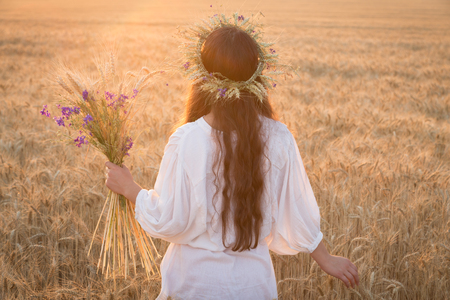 Girl walking with sheaf on wheat field at sunsetの写真素材