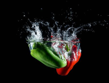 Red and green paprika falling in water on black backgroundの写真素材