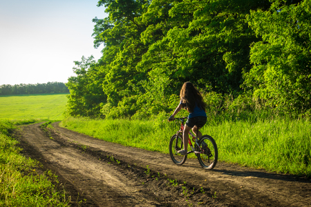 Young girl riding on the bike at country roadの写真素材