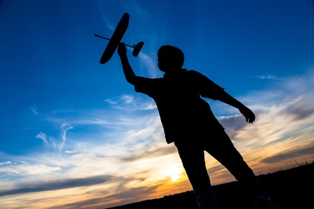 Silhouette of boy with his airplane against sunsetの写真素材