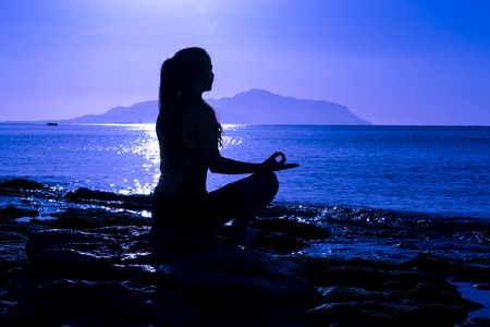 Silhouette of young girl meditating on the seaの写真素材