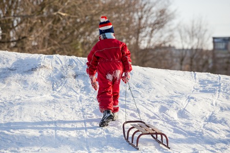 boy with sledge climbing at the snowy hill on winter park
