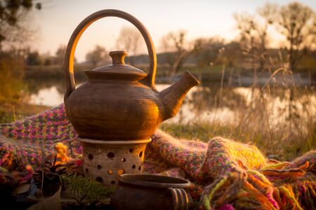 Hot teapot at autumn sunset on riverbankの写真素材