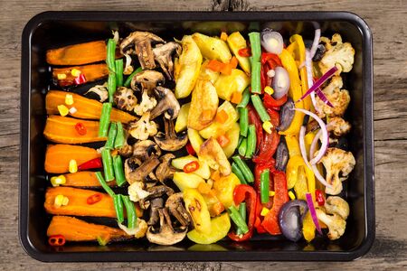 Chopped stewed vegetables on tray at wooden table, food background, flat layの写真素材