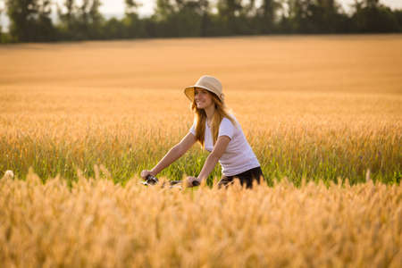 Young girl riding on bike at golden wheat field, summer vacation conceptの写真素材
