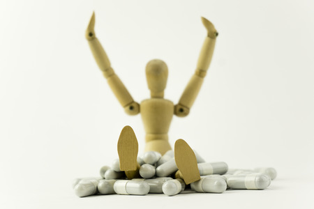 Wooden doll sitting in a pile of pills