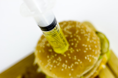 Syringe puming yellow liquid in a hamburger, on a white backgroundの写真素材