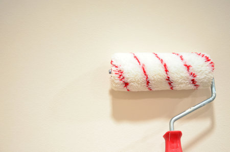 White paint roller on a decorative beige wall background. Interior design, repair and painting the walls yourself.の写真素材
