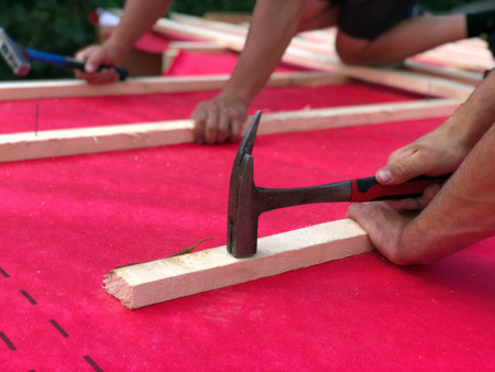 Construction roofers hammer nails on a waterproofing roof with hammers into wooden bars, making a rafter grate close-upの写真素材