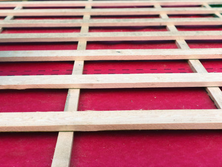 Roof lathing in a grid of edged wooden rafters and beams against the background of a protective...