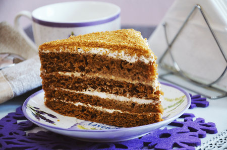 A piece of honey cake with cream on a table in a plate with a cup of coffeeの写真素材
