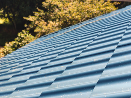 Blue metal tile on the roof of the house against the background of green trees in focusの写真素材